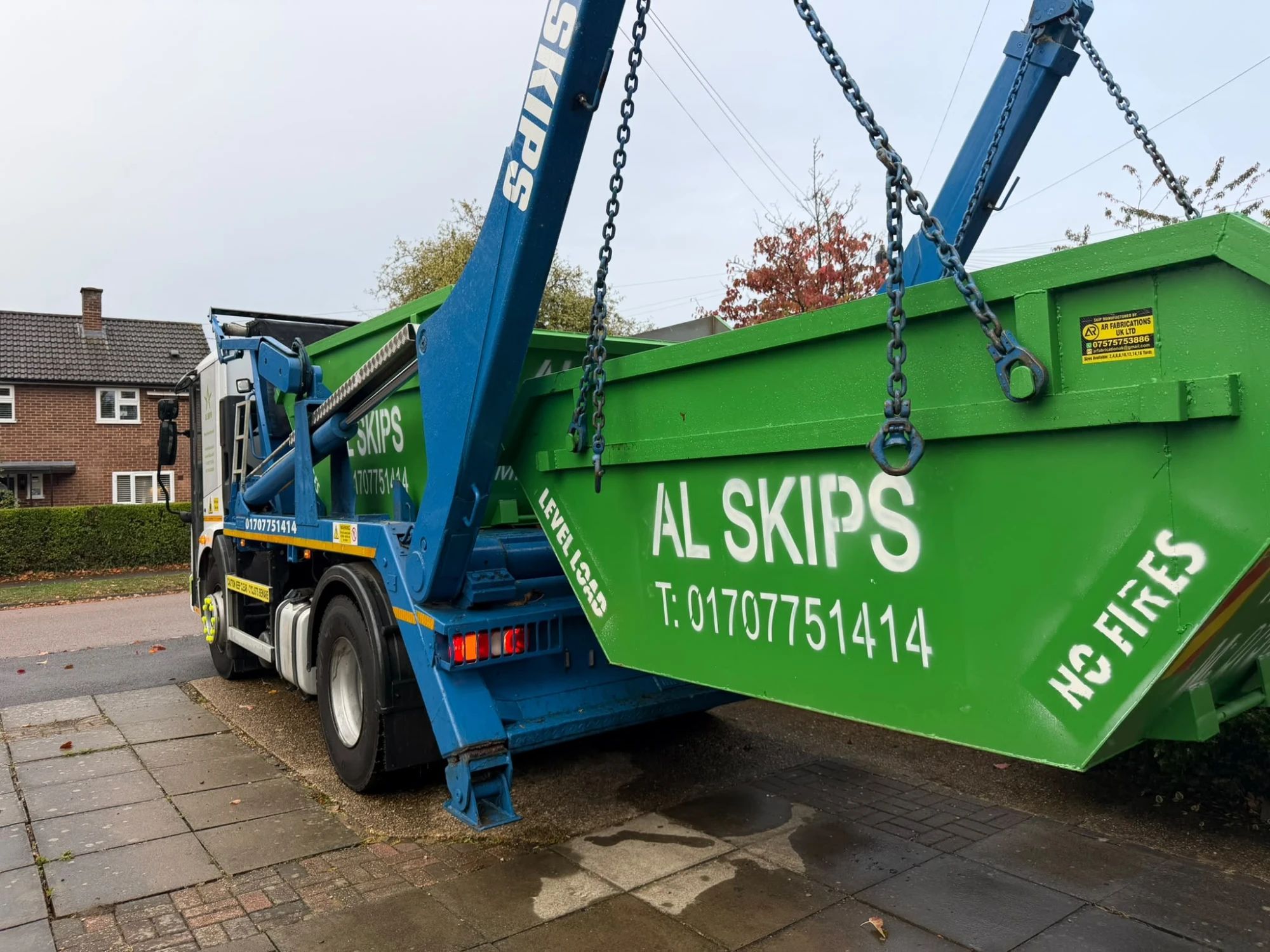 AL Skips lorry lifting a green skip at the roadside